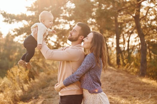 Happy family of mother, family and little baby rests outdoors. Beautiful sunny autumn nature.