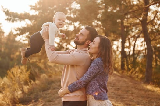 Happy family of mother, family and little baby rests outdoors. Beautiful sunny autumn nature.