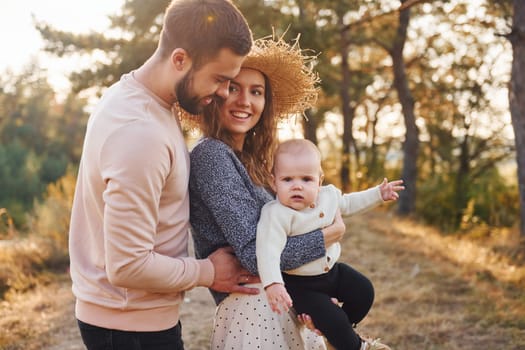 Happy family of mother, family and little baby rests outdoors. Beautiful sunny autumn nature.