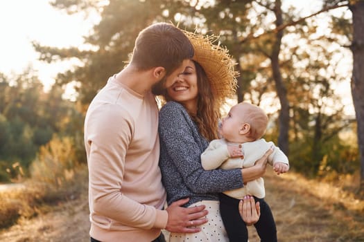 Happy family of mother, family and little baby rests outdoors. Beautiful sunny autumn nature.