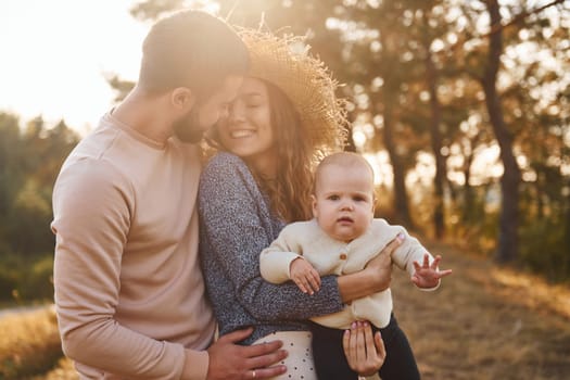 Happy family of mother, family and little baby rests outdoors. Beautiful sunny autumn nature.