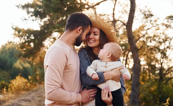 Happy family of mother, family and little baby rests outdoors. Beautiful sunny autumn nature.