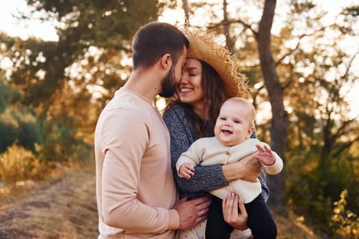 Happy family of mother, family and little baby rests outdoors. Beautiful sunny autumn nature.