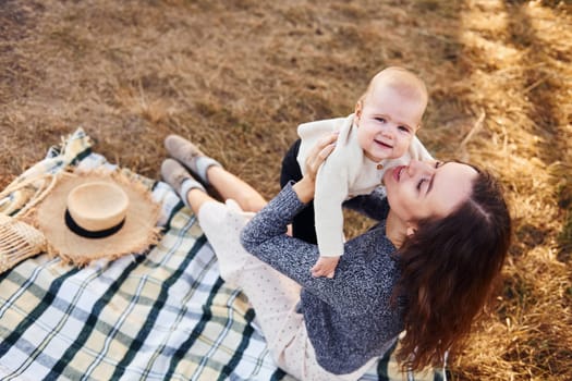 Young mother with her little baby rests outdoors at autumn season.