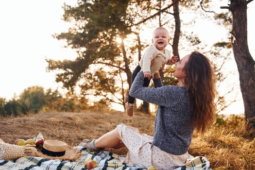 Young mother with her little baby rests outdoors at autumn season.
