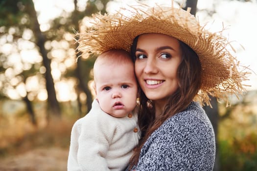 Young mother with her little baby rests outdoors at autumn season.