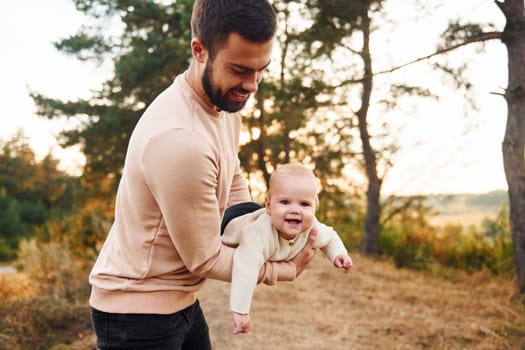 Bearded father playing with his child outdoors at sunny daytime outdoors.