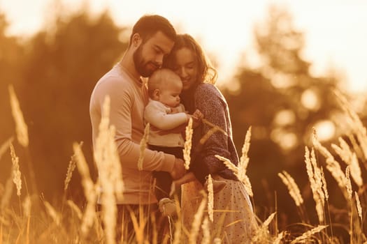 Illuminated by sunlight. Happy family of mother, family and little baby rests outdoors. Beautiful sunny autumn nature.