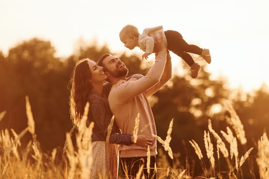 Illuminated by sunlight. Happy family of mother, family and little baby rests outdoors. Beautiful sunny autumn nature.