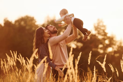 Illuminated by sunlight. Happy family of mother, family and little baby rests outdoors. Beautiful sunny autumn nature.