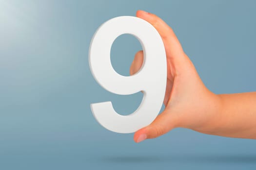 Number nine in hand. A hand holds a white number 9 on a blue background. Concept with number nine. Birthday 9 years, percentage, ninth grade or day