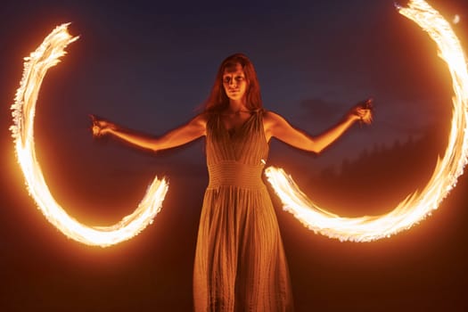 Photo with a long exposure. Fire show by woman in dress in night Carphatian mountains. Beautiful landscape.
