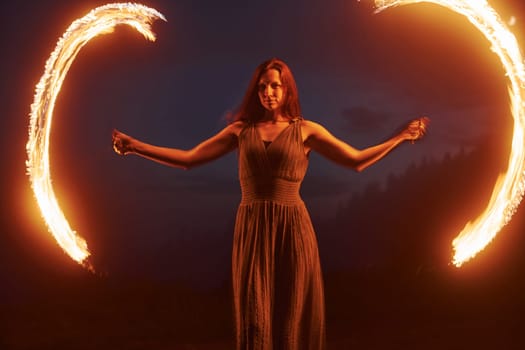 Photo with a long exposure. Fire show by woman in dress in night Carphatian mountains. Beautiful landscape.