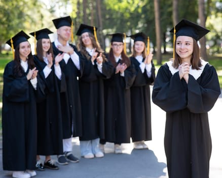 Group of happy students in graduation gowns outdoors. A young girl in the foreground