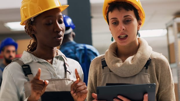 Depot managers in overalls using tablet for inventory, planning distribution and logistics for delivery service. Team of diverse people checking stock products in storage room. Handheld shot.