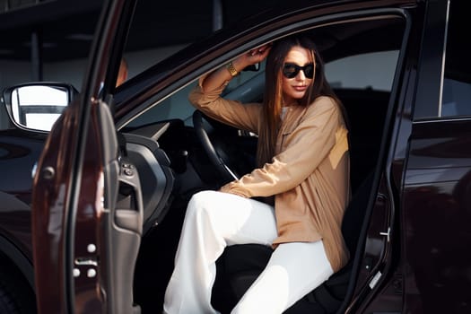 Sits with car's window opened. Fashionable beautiful young woman and her modern automobile.