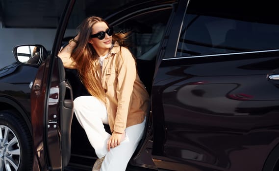 Enjoying fresh air. Fashionable beautiful young woman and her modern automobile.