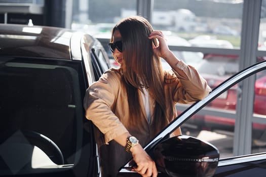 Standing near opened window. Fashionable beautiful young woman and her modern automobile.