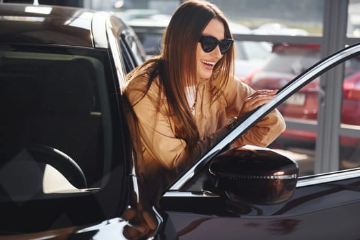 Standing near opened window. Fashionable beautiful young woman and her modern automobile.