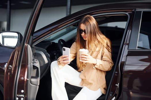 Coffee break. Fashionable beautiful young woman and her modern automobile.