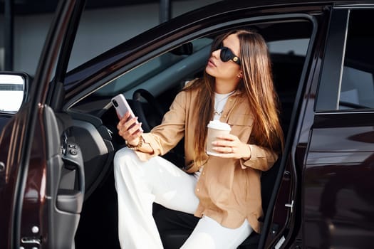 Coffee break. Fashionable beautiful young woman and her modern automobile.