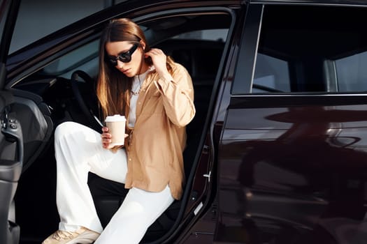 Coffee break. Fashionable beautiful young woman and her modern automobile.