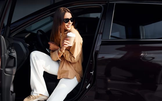 Coffee break. Fashionable beautiful young woman and her modern automobile.