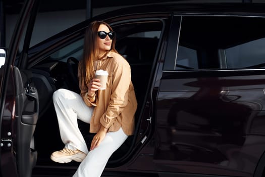 Coffee break. Fashionable beautiful young woman and her modern automobile.