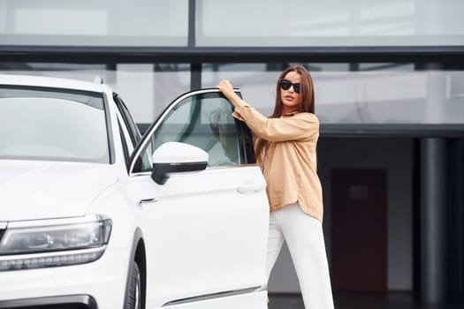 Outside near car. Fashionable beautiful young woman and her modern automobile.