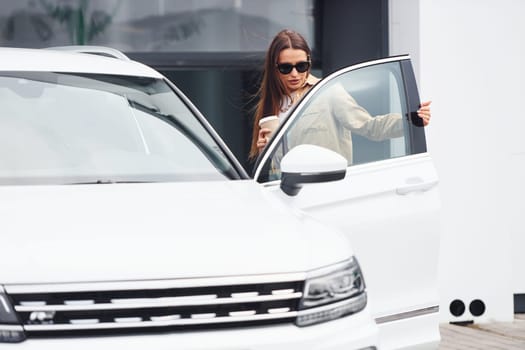 Outside near car. Fashionable beautiful young woman and her modern automobile.