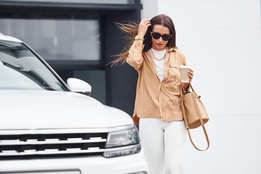 Outside near car. Fashionable beautiful young woman and her modern automobile.