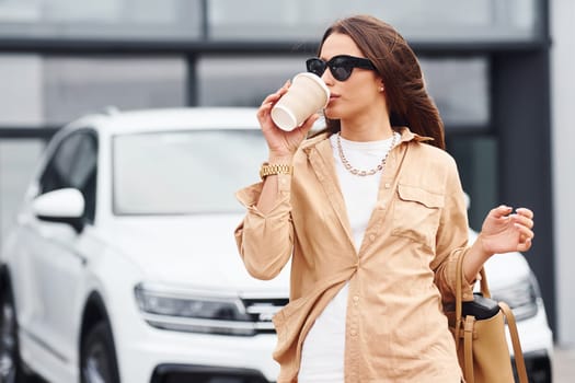 Outside near car. Fashionable beautiful young woman and her modern automobile.