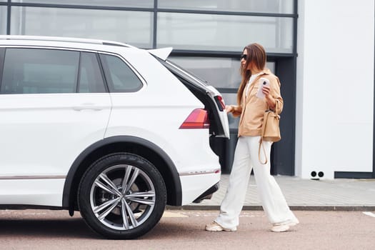 Outside near car. Fashionable beautiful young woman and her modern automobile.