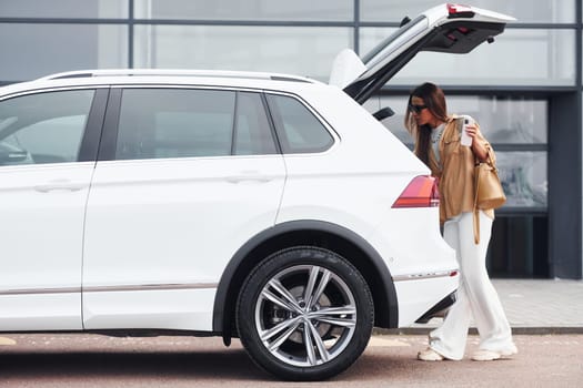 Outside near car. Fashionable beautiful young woman and her modern automobile.