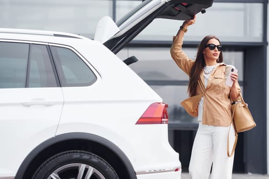 Outside near car. Fashionable beautiful young woman and her modern automobile.