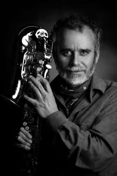 shot of a male musician, saxophonist, holding a saxophone alto jazz musical instrument and thinking, isolated on a dark background. High quality photo