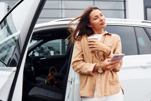 With coffee and phone. Fashionable beautiful young woman and her modern automobile.