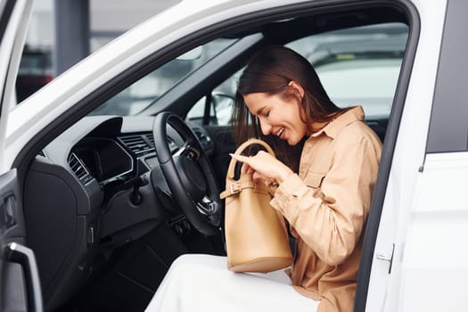 Serching something in bag. Fashionable beautiful young woman and her modern automobile.