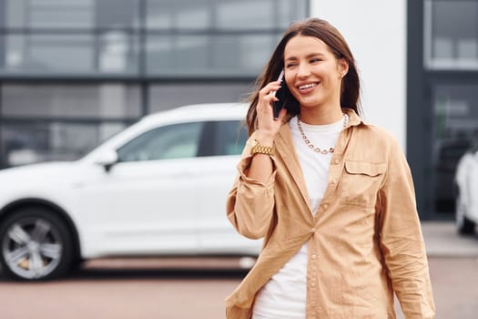 Walks nearby car. Fashionable beautiful young woman and her modern automobile.