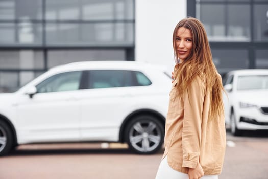 Walks nearby car. Fashionable beautiful young woman and her modern automobile.