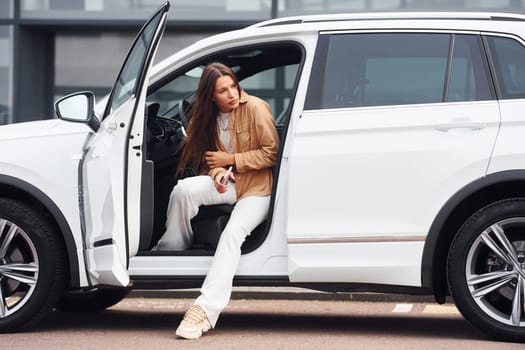 Looks outside from the car. Fashionable beautiful young woman and her modern automobile.