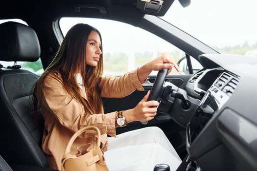 Side view of fashionable beautiful young woman that is inside her modern automobile.