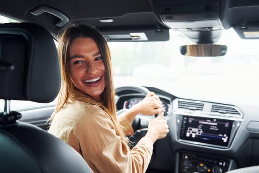 Driver looks back and smiling. Fashionable beautiful young woman and her modern automobile.