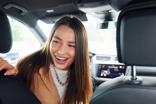 Driver looks back and smiling. Fashionable beautiful young woman and her modern automobile.