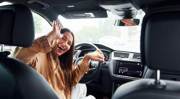 Driver looks back and smiling. Fashionable beautiful young woman and her modern automobile.