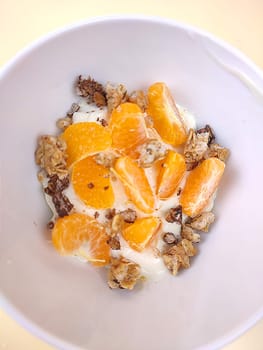 Bowl of yogurt with sliced orange and granola, close up over cream background. Studio shot