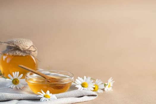 Chamomile syrup in a small bowl and in a jar and chamomile flowers on a linen kitchen towel, copy space.