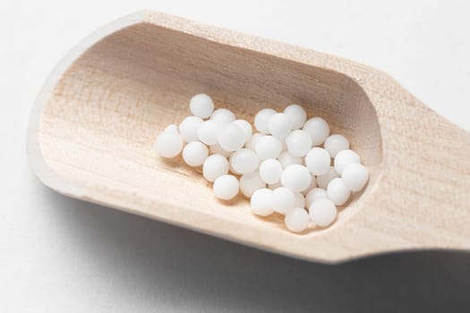 White homeopathic granules on a small wooden scoop.