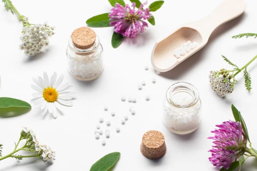 Composition of homeopathic medicines and medicinal plants on a white table.