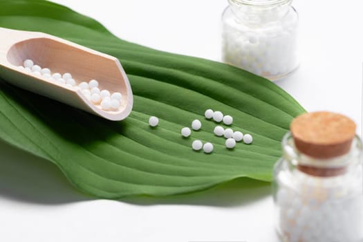 Homeopathic pills scattered from a wooden scoop on a green leaf.